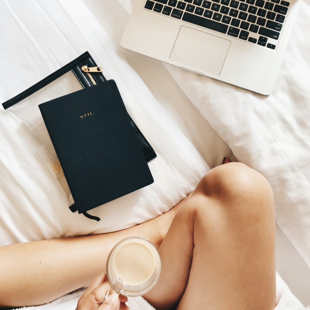 Girl siting on the bed with coffee and some notebooks and a Mac. 