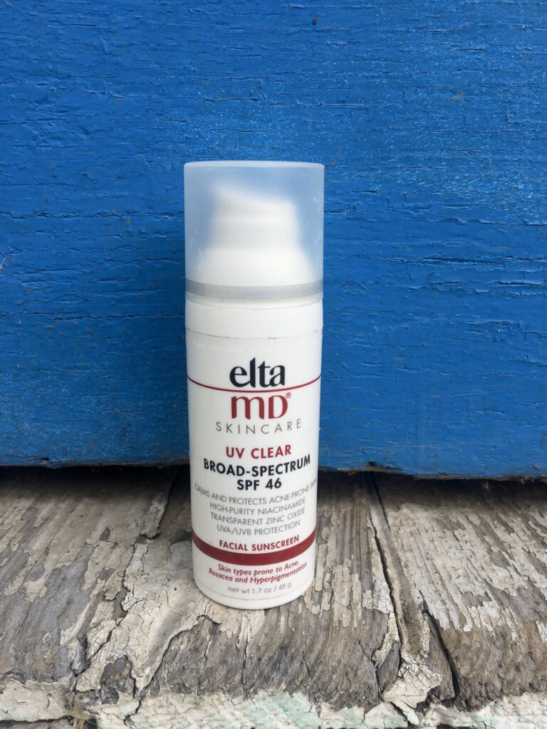EltaMD Sunscreen in front of a blue door with older wooden floor boards at the bottom. 