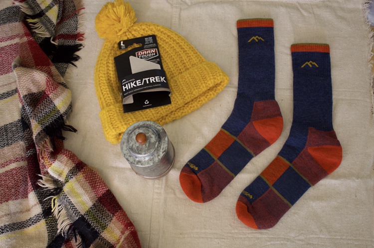 Yellow hat and a candle laid out with a pair of Darn Tough socks. 