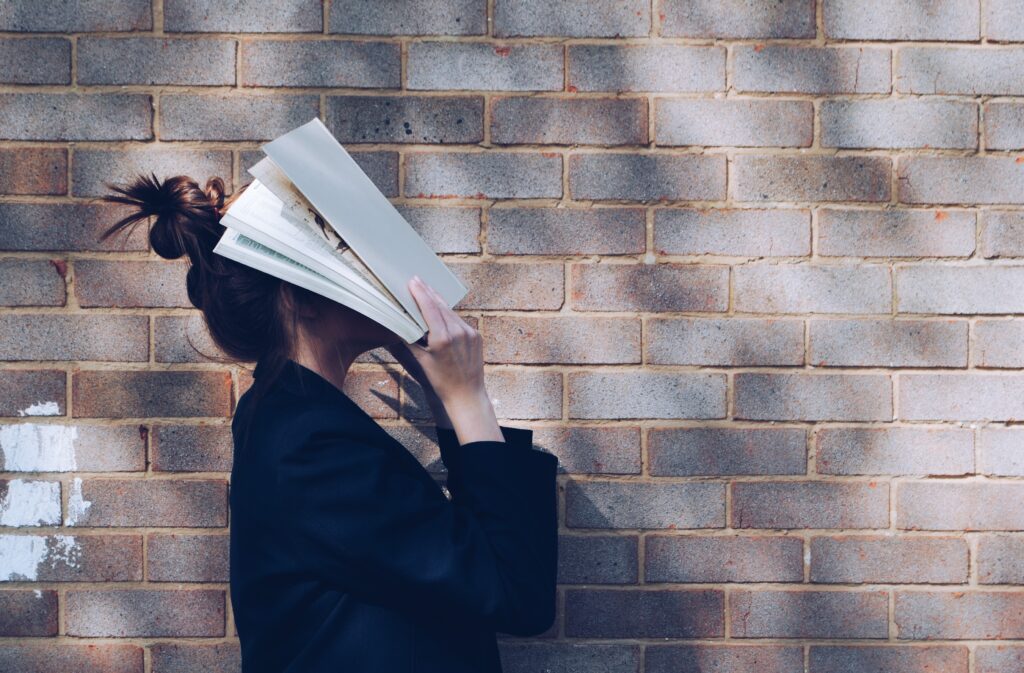 Girl with her hair in a bun and her face in a book against a brick wall background. Funny ways to save money.