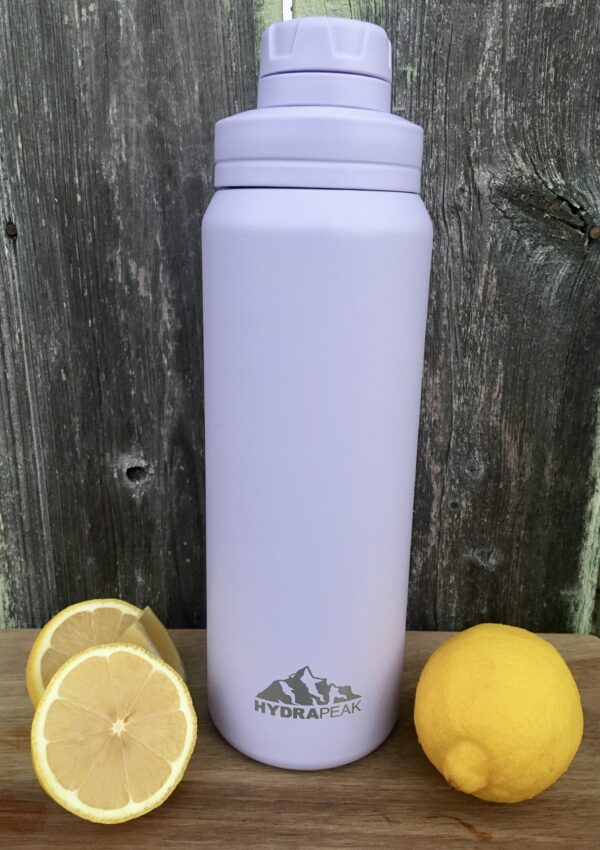 A light purple water bottle sitting on a wooden board with a fence in the background and lemons on either side. Hydrapeak water bottle review.