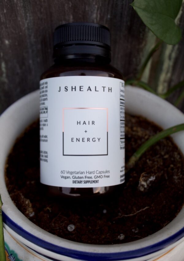 JSHealth Hair and Energy bottle sitting in a plant pot.