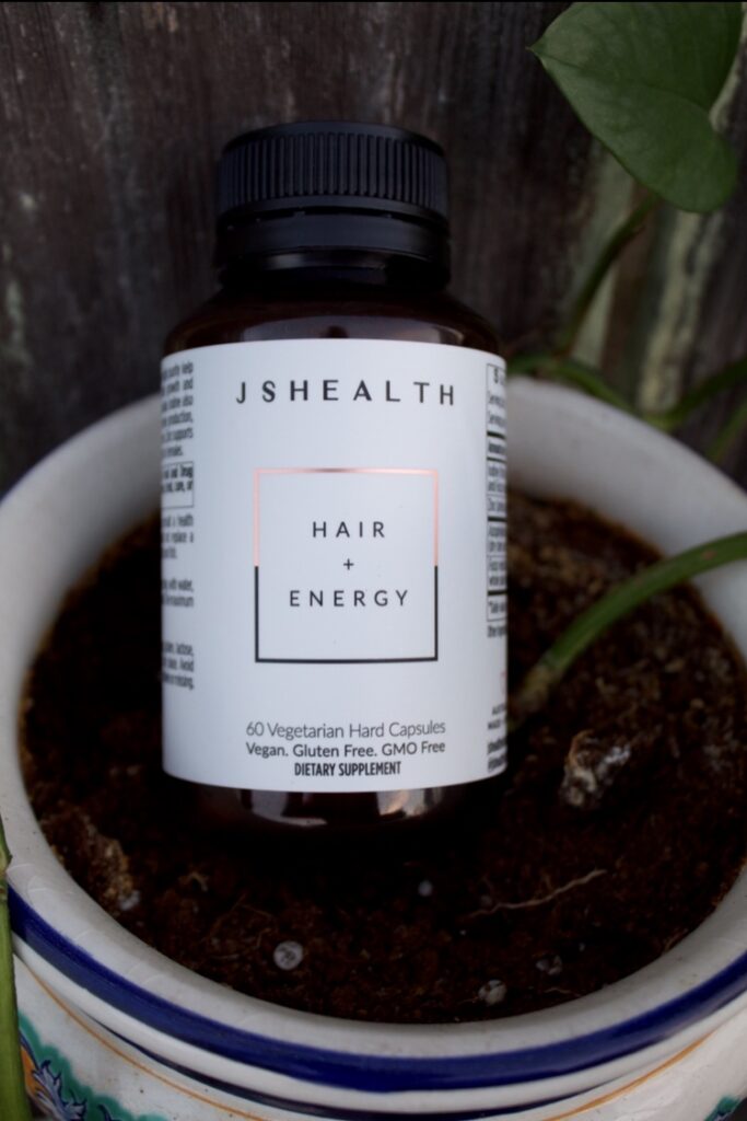 JSHealth Hair and Energy bottle sitting in a plant pot. 