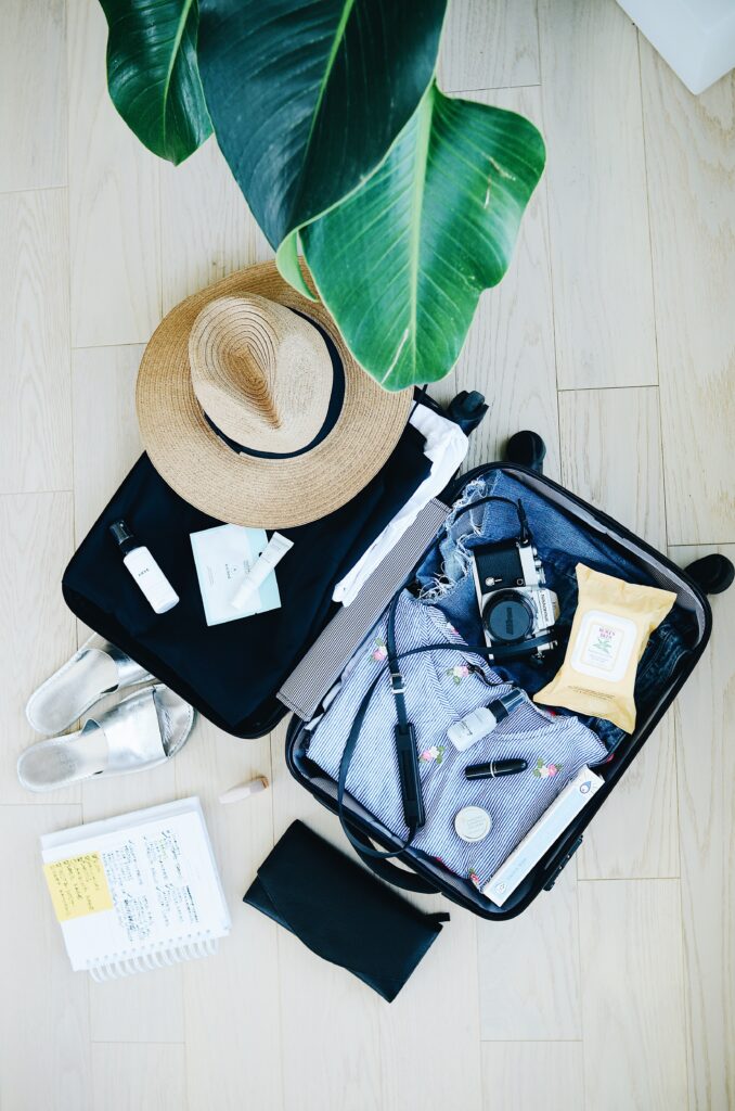 A green house plant leaning over an open suitcase that is packed with a vacation style hat sitting on top. The perfect get-away vibe for the Discover It Miles vs. Discover It cash back discussion.