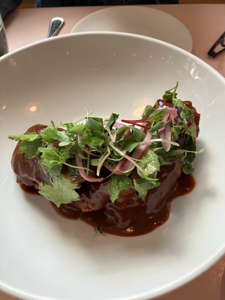 Fried eggplant covered in a dark brown sauce and topped with fresh herb sprouts at Cafe Roze
