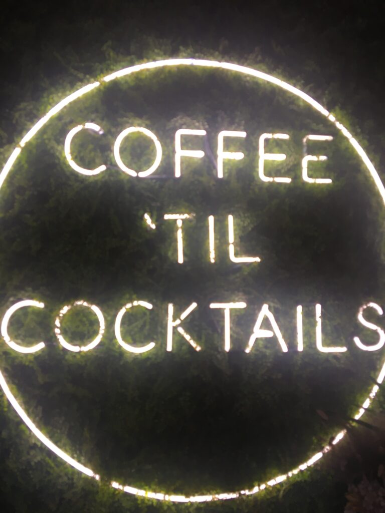 A green background with a light up light that says Coffee til Cocktails. Picture from Parlor Public house during a Weekend in Indianapolis. 