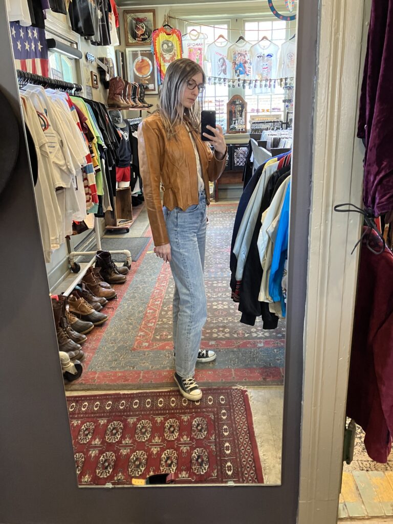 Girl taking a mirror pic wearing a vintage 70s leather jacket while thrifting in Nashville. 