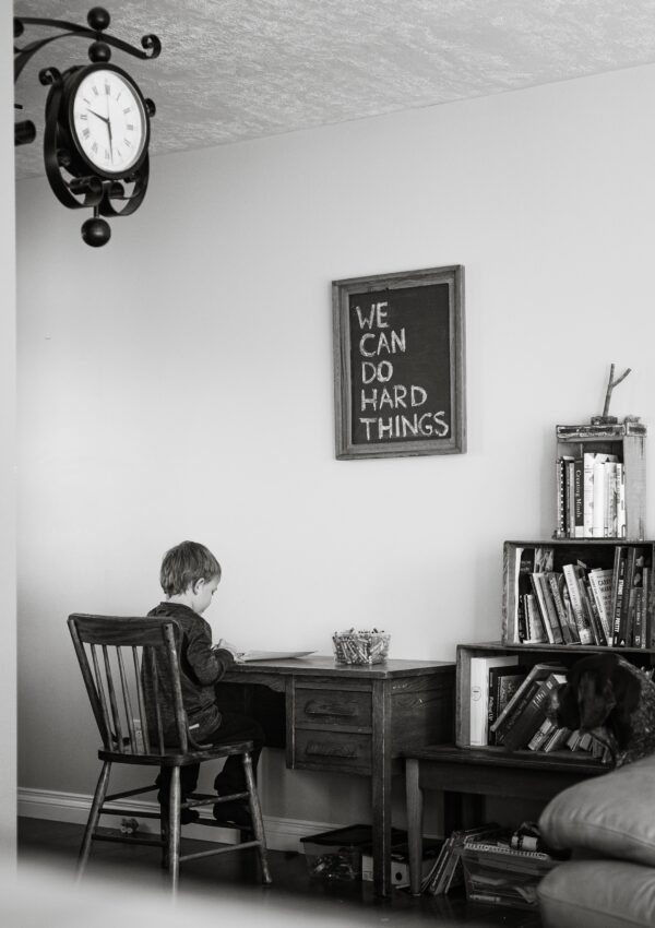 You're not doing enough. A little boy sitting at a desk doing school work with a sign that says we can do hard things.