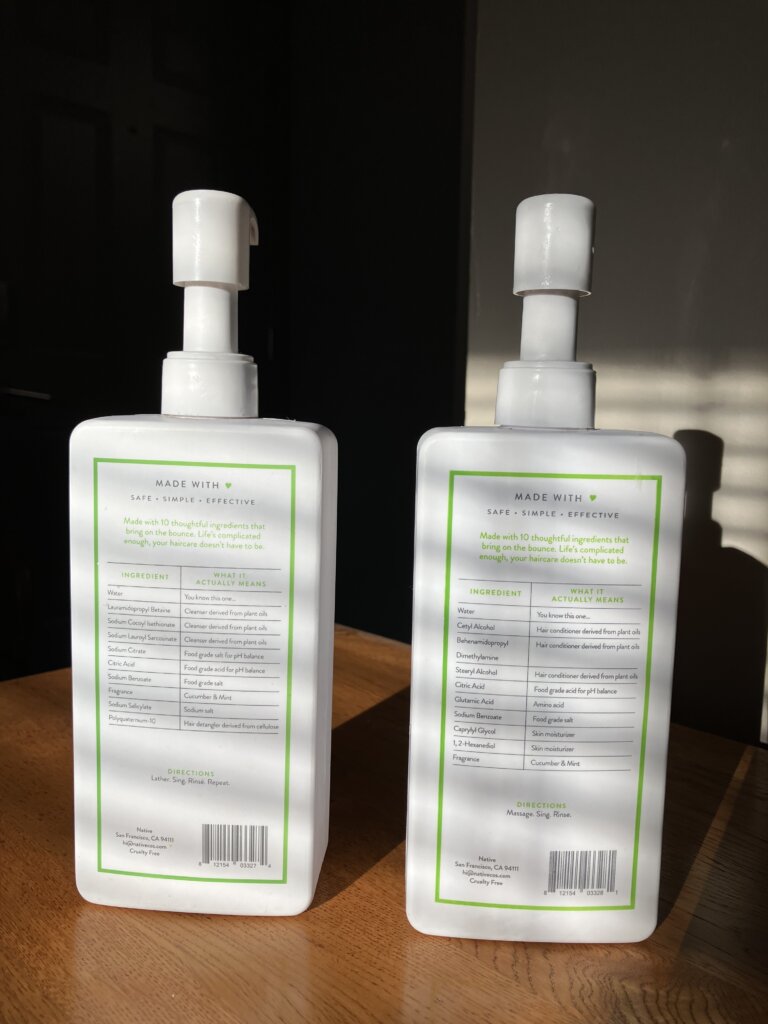 Native shampoo and conditioner bottles with ingredients list facing the camera in the morning light sitting on a wooden table. 