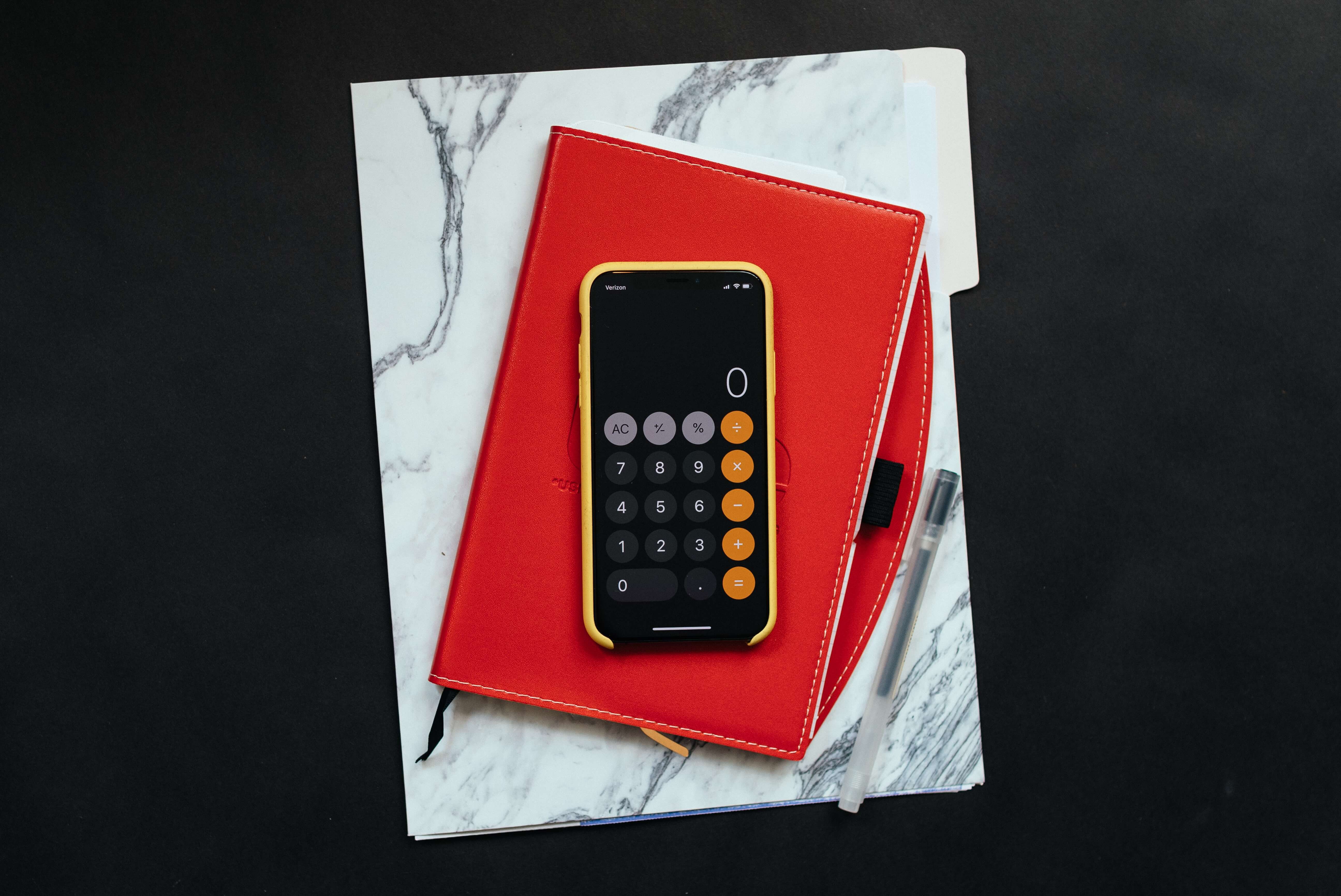 An iPhone with the calculator app open on top of a red notebook and marble folder. What is an emergency fund. 