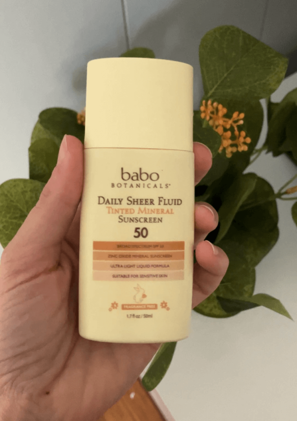 Babo Botanicals sunscreen being held infant of a fake plant.