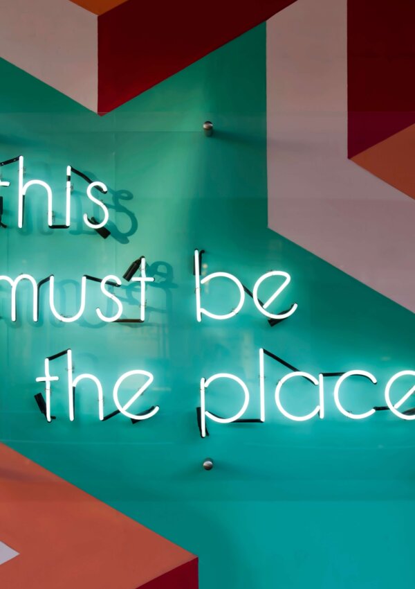 A neon sign that says 'this must be the place'. Title photo for a blog post about tips for starting a new job.